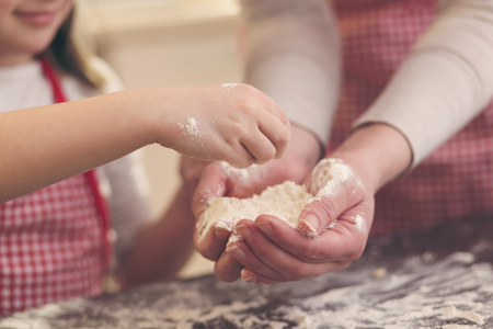 Detail of mother and daugther baking cookies, playing with flour on the kitchen counter. Selective focus on the fingersの写真素材