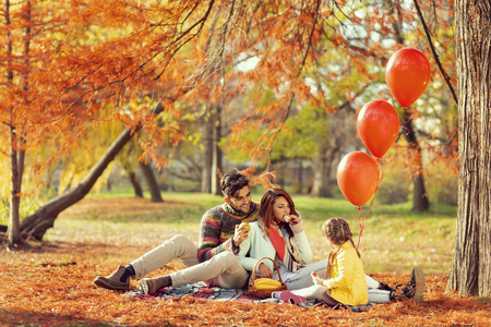 Young family sitting on a picnic blanket, eating sandwiches, having fun and enjoying a beautiful autumn day in natureの写真素材
