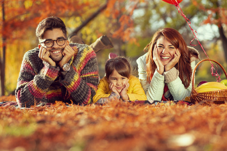Beautiful mother, father and daughter having fun on an autumn picnic in park; family enjoying sunny autumn day in natureの写真素材