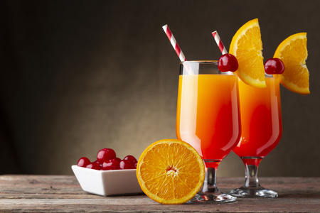 Two cold tequila sunrise cocktails with tequila, pomegranate juice and orange juice decorated with slices of orange and maraschino cherriesの写真素材