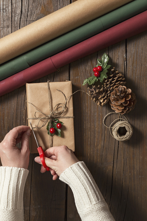 Top view of female hands wrapping Christmas presents on wooden table backgroundの写真素材