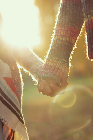 Detail of a young couple in love holding hands and walking through a park on a sunny autumn dayの写真素材