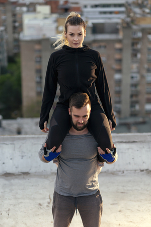 Couple working out on a building rooftop terrace, man carrying woman on his shoulders and doing squatsの写真素材