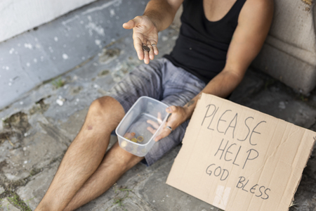 High angle view of a homeless man sitting on the street, begging for money. Focus on the coin in the handの写真素材
