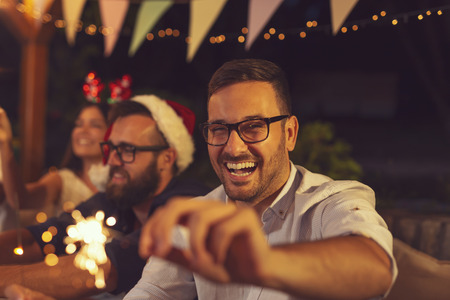 Friends having fun at an outdoor New Year's Eve party, dancing, drinking and waving with sparklers at midnight countdownの写真素材