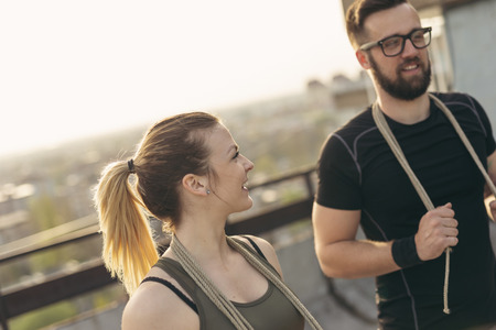 Couple standing on a building rooftop terrace, getting ready for exercising with ropes. Focus on the girlの写真素材