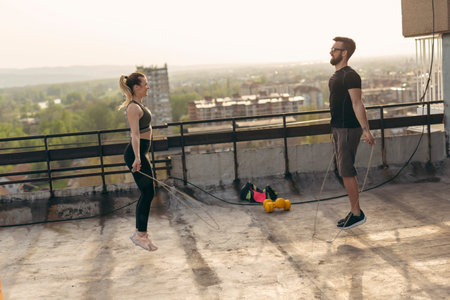 Couple exercising on a building rooftop terrace, jumping ropes; urban skyline in the background