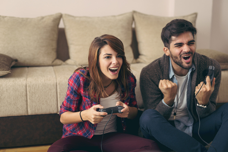Couple in love enjoying their free time, sitting on the living room floor, playing video games and having fun. Focus on the womanの写真素材
