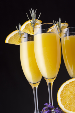 Mimosa cocktails in champagne glasses with orange juice and sparkling wine decorated with lavender leaves and orange slices. Focus on the lavender leaves on the glassの写真素材