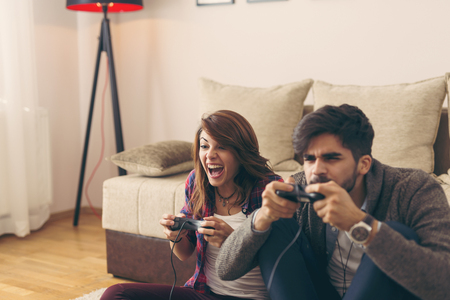 Couple in love enjoying their free time, sitting on the living room floor, playing video games and having fun. Focus on the womanの写真素材