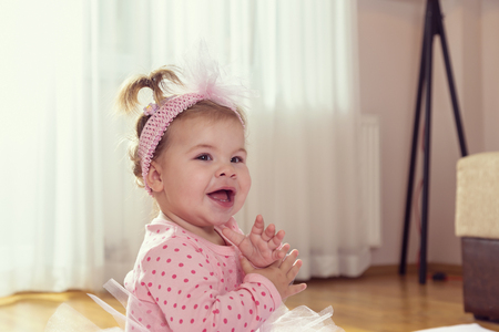 Beautiful little baby girl sitting on a duvet on living room floor, smiling and clapping handsの写真素材