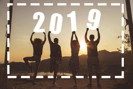 Silhouette of a group of friends standing near a seaside cliff, holding numbers 2019 and looking at a beautiful sunset at Valtos beach in Parga, Greeceの写真素材