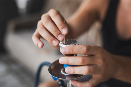 Detail of male hands punching holes in tinfoil placed over a fruity flavored, molasses based hokkah tobacco using a toothpick, getting it ready for use. Selective focus on the fingersの写真素材