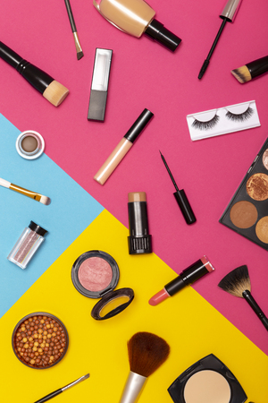 Flat lay of various make up products on colorful background. Make up brushes, blushes, face powders, corrector, highlighters, lip gloss, lipstick, mascara, eyeliner and eyelashesの写真素材