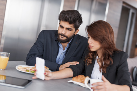 Two colleagues having breakfast and discussing work related matters in company's restaurant. Focus on the manの写真素材