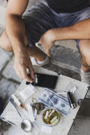 Detail of male hands cutting heroin line with a razor blade on a smart phone screen, getting it ready for useの写真素材