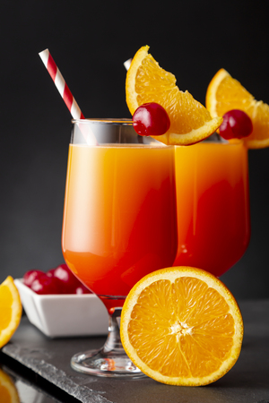 Two cold tequila sunrise cocktails with tequila, pomegranate juice and orange juice decorated with slices of orange and maraschino cherriesの写真素材