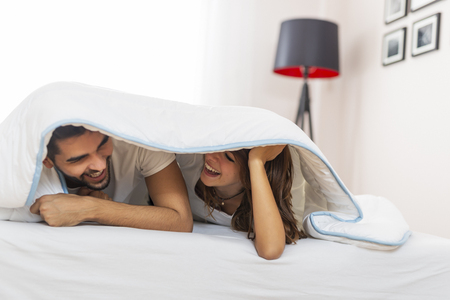 Couple in love lying under the sheets, peeking and laughingの写真素材