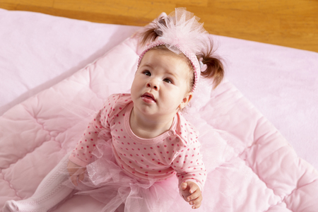 High angle view of a beautiful baby girl wearing pink tutu skirt sitting on a pink duvet, looking up and smilingの写真素材