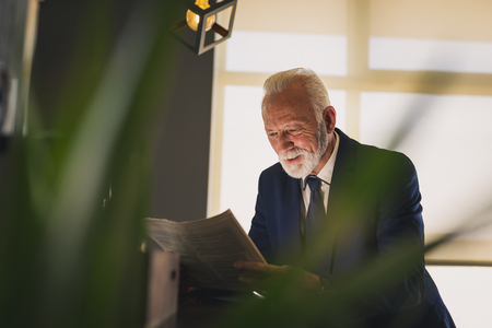 Senior businessman standing next to a counter in a cafe, reading newspaperの写真素材