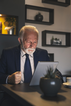 Senior businessman in a restaurant, working on a tablet computer, pensive and seriousの写真素材