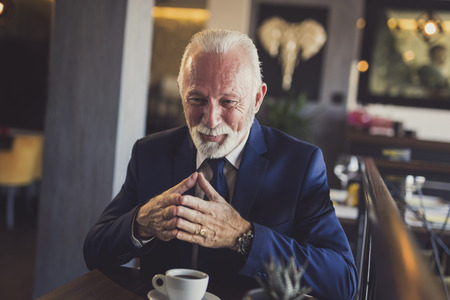Senior businessman on a meeting in a restaurant, having a conversation with business partner and drinking coffeeの写真素材