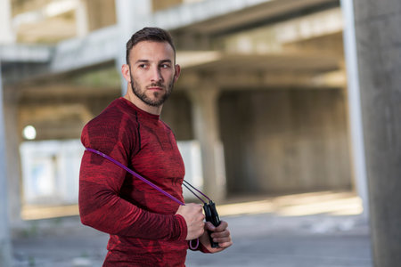 Athletic, muscular man taking a workout break, standing and holding a jumping rope
