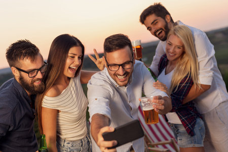 Group of friends having fun at an outdoor summertime party, dancing, drinking beer and taking...