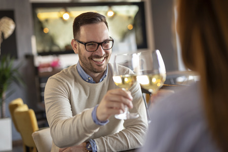 Young couple in love on a date, sitting at a restaurant table, raising glasses of wine and making a toastの写真素材