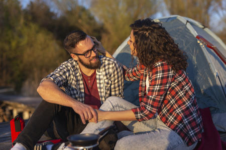 Couple in love camping at the lake docks, sitting in front of a tent, hugging and enjoying a beautiful sunny day in natureの写真素材