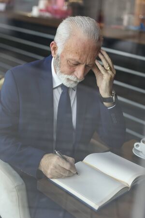 Senior businessman working, taking notes in a planner, serious and pensiveの写真素材