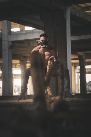 Athletic, muscular man wearing training mask and doing battle ropes functional training, making waves with the ropes, exercising strengthの写真素材