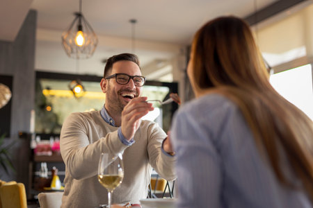 Couple in love on a date, having lunch at a restaurant, drinking wine and having fun tasting each others foodの写真素材