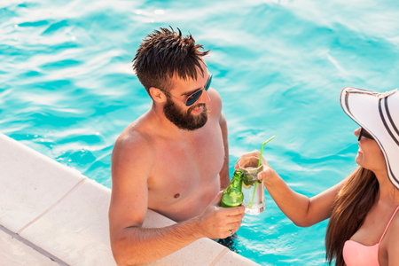 Couple in love having fun at a poolside summer party, standing in water next to the swimming pool...