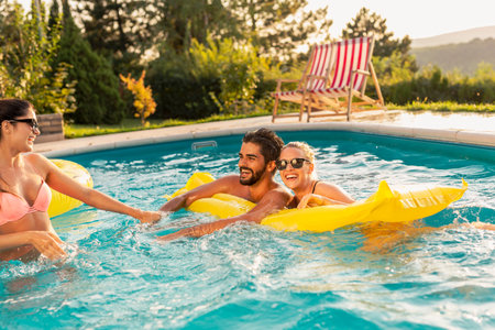 Group of friends at a poolside summertime party,  having fun in the swimming pool, sunbathing on a...