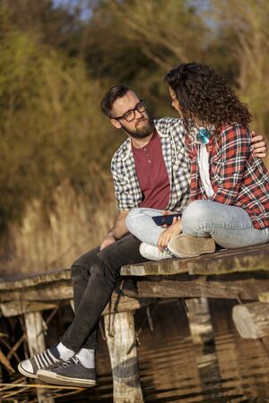 Young couple in love sitting at a lake docks,  enjoying a beautiful sunset over the lakeの写真素材