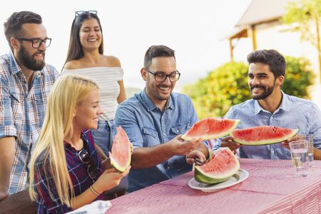 Group of friends having an outdoor lunch, eating fresh watermelon slices and having funの写真素材