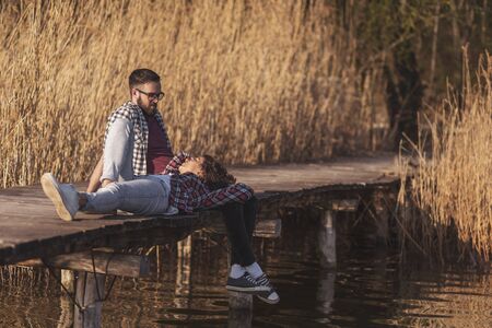 Couple in love enjoying a beautiful sunny autumn day in nature, relaxing at lake docksの写真素材