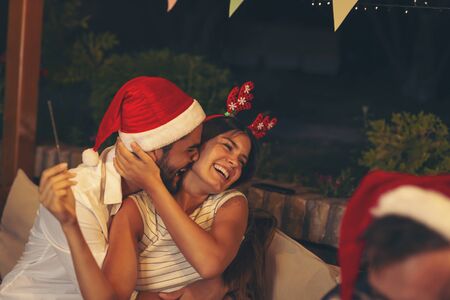 Couple having fun at an outdoor New Year's Eve party, waving with sparklers and kissing at midnight countdownの写真素材