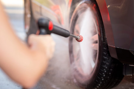 Detail of female hands washing a car tires with hot hight pressure water and detergent