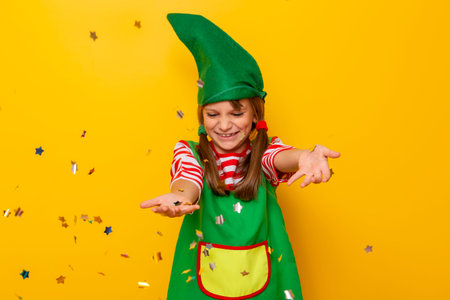 Portrait of a beautiful little girl dressed as a Christmas elf, having fun while throwing colorful...