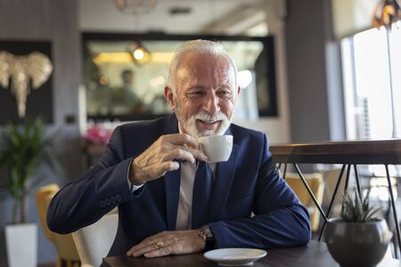 Senior businessman on coffee break in a restaurant, having a conversation with business partner and drinking coffeeの写真素材