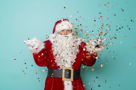 Santa Claus celebrating New Year and having fun, isolated on mint colored background with colorful confetti all aroundの写真素材