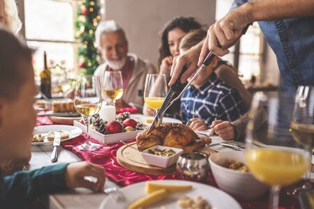 Family having a Christmas dinner at home, enjoying their time together, talking to each other, laughing and cutting the chickenの写真素材