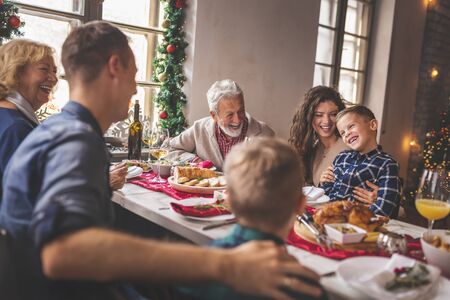 Beautiful happy family gathered around the table, having Christmas dinner, enjoying their time together and the winter holiday seasonの写真素材