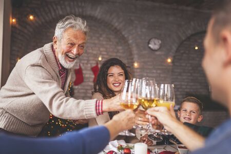 Beautiful happy family gathered around the table, having Christmas dinner all together at home, celebrating Christmas and making a toastの写真素材