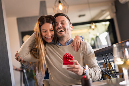 Couple on a date in restaurant, celebrating man's birthday; woman giving man his birthday present...