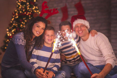 Beautiful happy family celebrating Christmas Eve at home, sitting by a nicely decorated Christmas tree, having fun while holding sparklersの写真素材