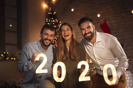 Group of young friends having fun at New Years party, holding illuminative numbers 2020 representing the upcoming New Year at midnight countdownの写真素材