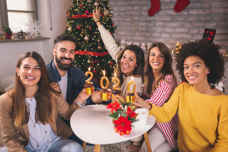 Group of young friends celebrating Christmas at home, holding cupcakes with lit candles shaped as...